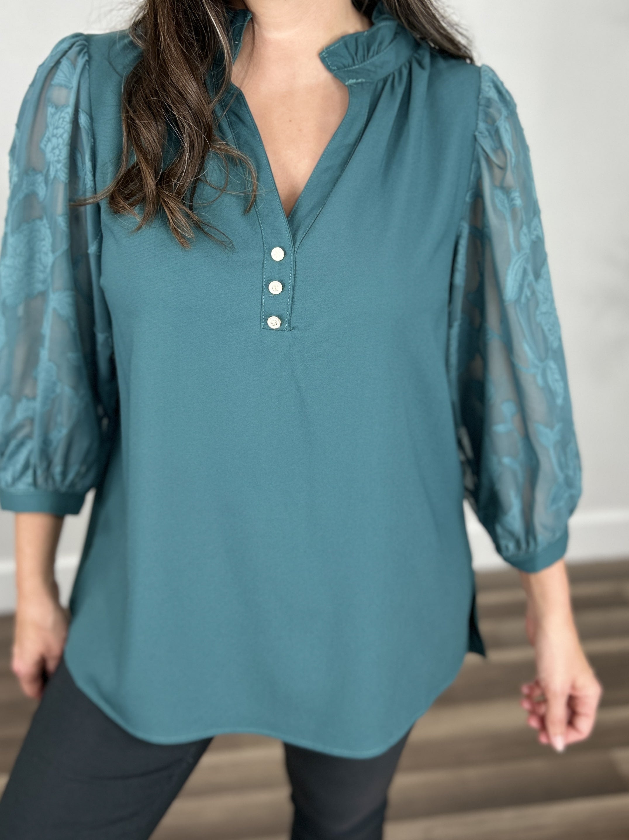 Upclose view of the women's teal three quarter sheer sleeve top with v neckline and decorative flower button detail.