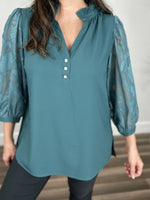 Load image into Gallery viewer, Upclose view of the women&#39;s teal three quarter sheer sleeve top with v neckline and decorative flower button detail.
