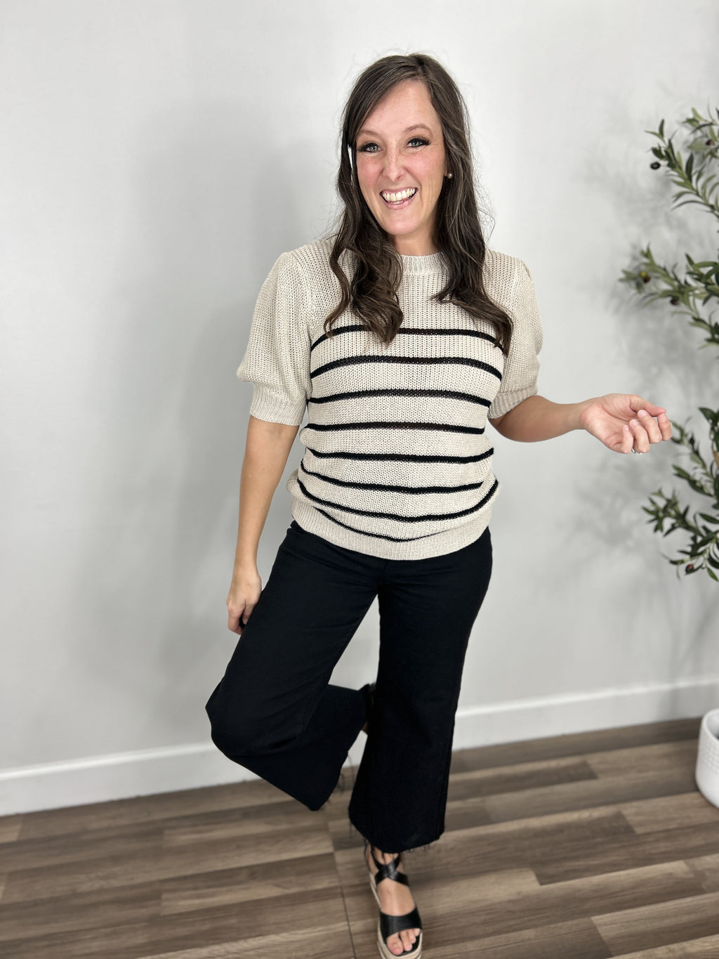 Women's taupe and white striped knit sweater top styled with black denim pants and black wedge sandals.