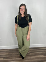 Load image into Gallery viewer, Women&#39;s green jumpsuit with suspender straps paired with black t-shirt and black mule slides.
