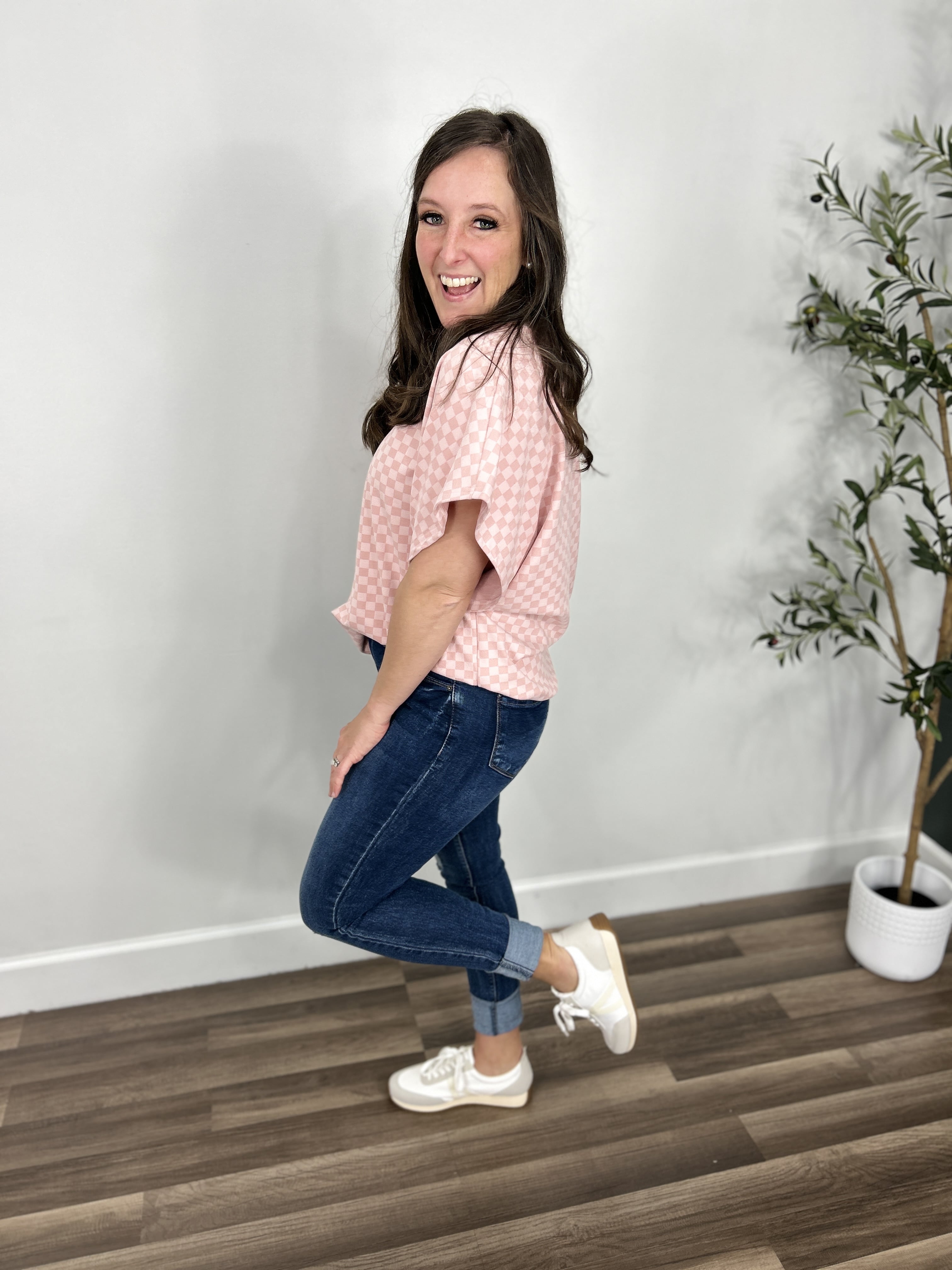 Side view of women's two tone pink checker print top paired with blue jeans and white sneakers.