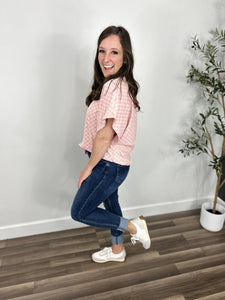 Side view of women's two tone pink checker print top paired with blue jeans and white sneakers.