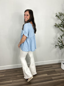 Back view of the Desi V Neck short sleeve oversized top styled with white frayed hem flare pants and black wedge sandals.
