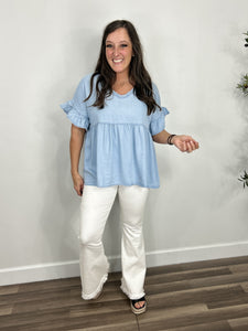 Women's chambray v neck short sleeve oversized top paired with white flare pants and black wedge sandals.