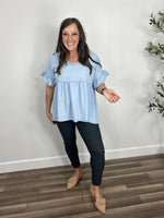 Load image into Gallery viewer, Women&#39;s chambray babydoll top with a modest v neck paired with charcoal skinny jeans and flat camel slides.
