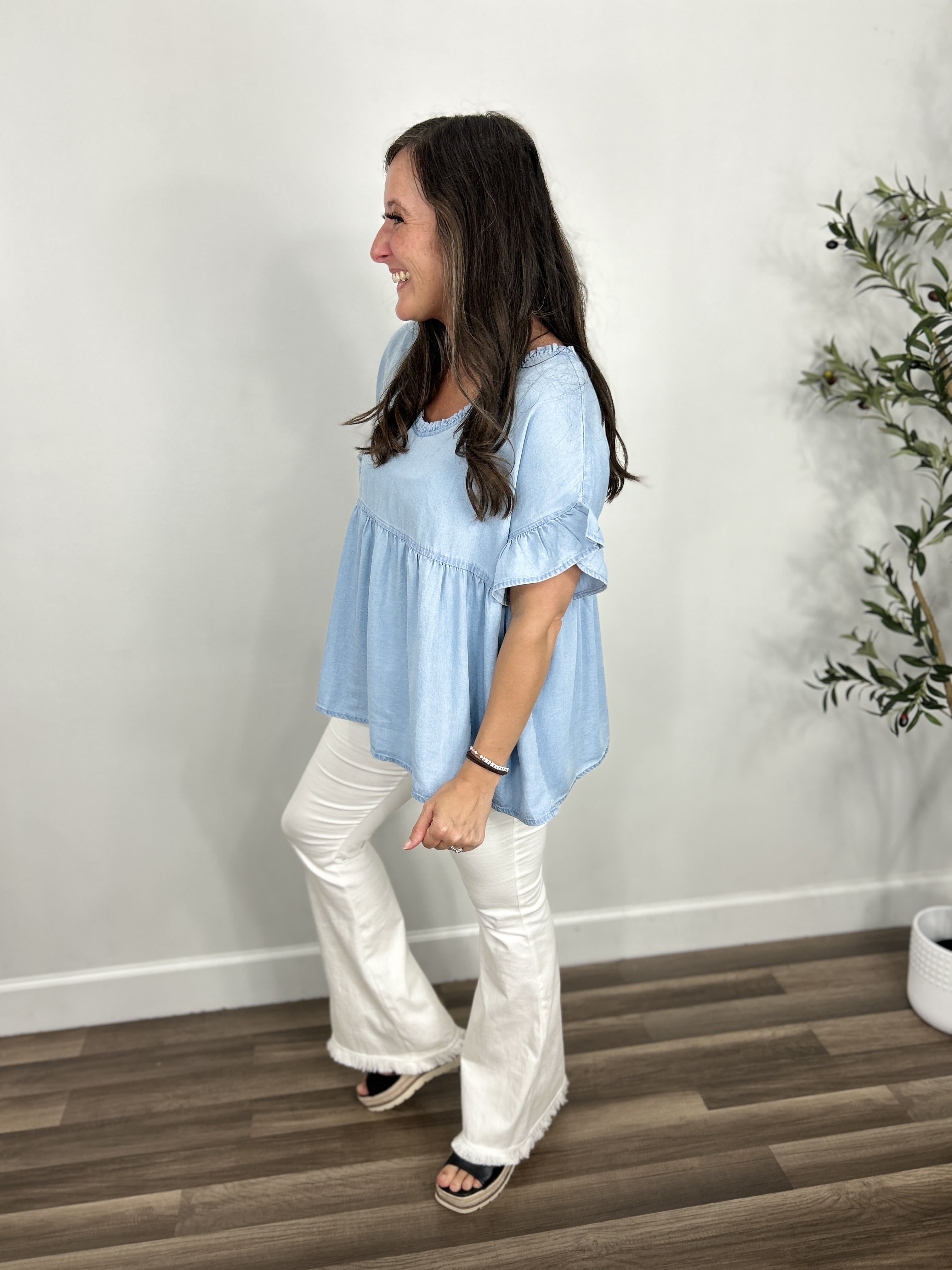 Women's chambray v neck short sleeve babydoll top paired with white flare pants and black sandals.