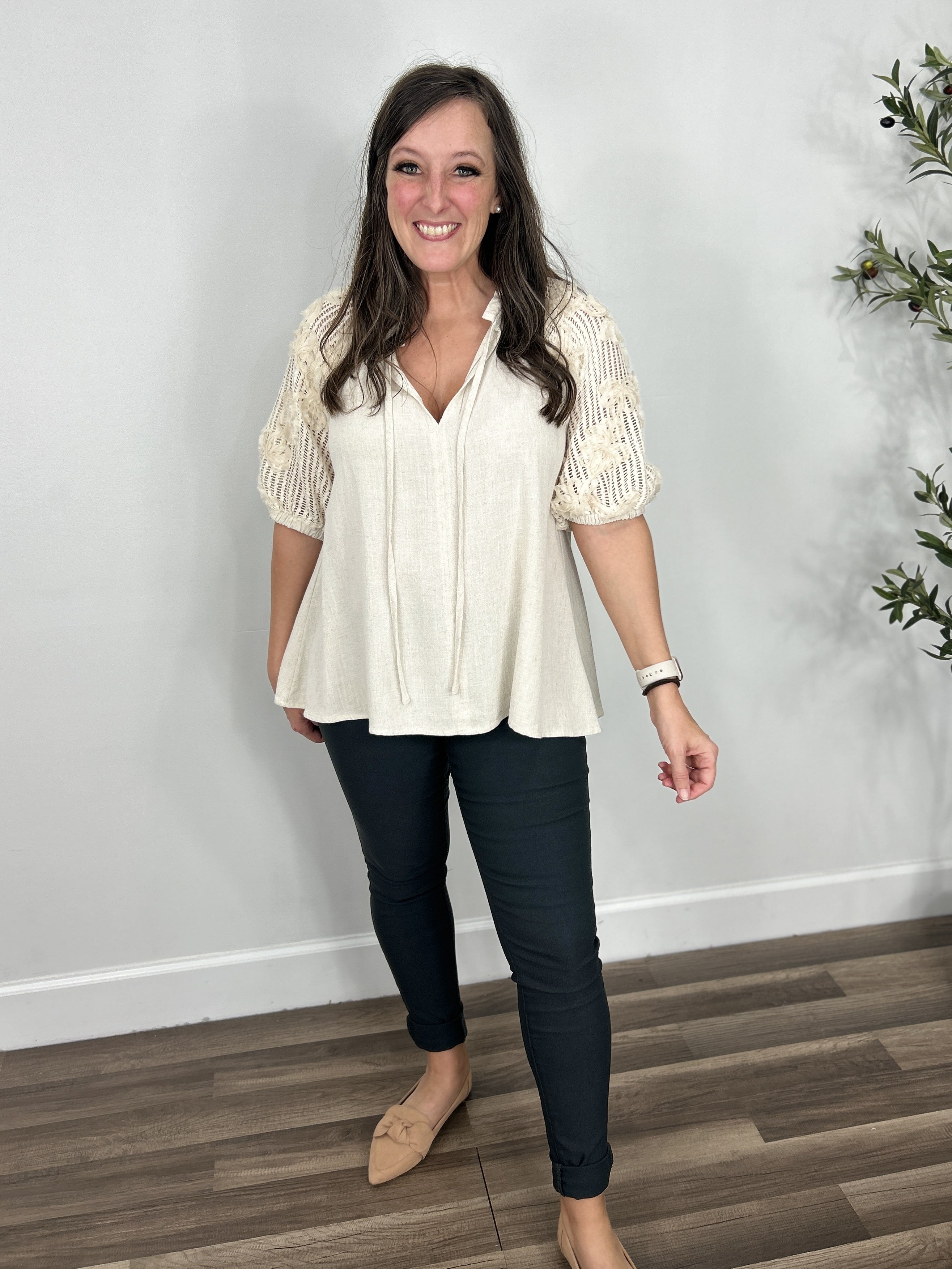 Women's oatmeal color v neck top with crochet short sleeves paired with charcoal skinny jeans and flat camel color shoes.