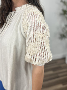 Women's linen blend top upclose view of crochet sleeve with flower detailing.