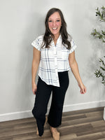 Load image into Gallery viewer, Women&#39;s blue and white plaid design short sleeve top half tucked into a pair of black denim.
