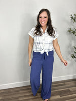 Load image into Gallery viewer, Women&#39;s Franklin Plaid Button Down Top with short sleeves and fold over collar tied in a front knot paired with blue wide leg pants.
