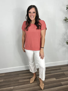 Women's coral color round neck short sleeve top paired with white crop flare pants and flat shoes.