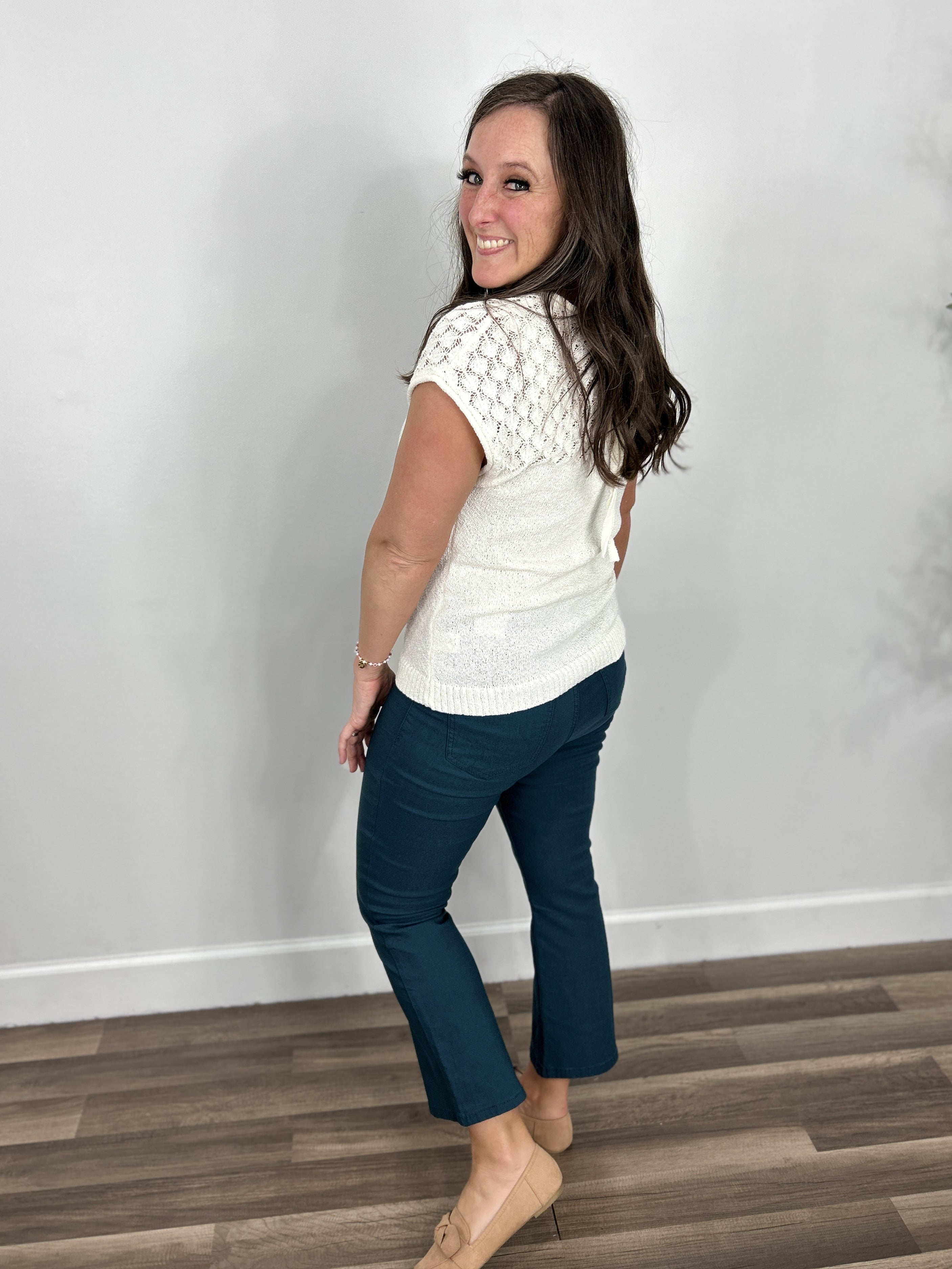 Back view of the Gracelynn cap sleeve sweater top in ivory paired with teal crop pants and camel color flat shoes.