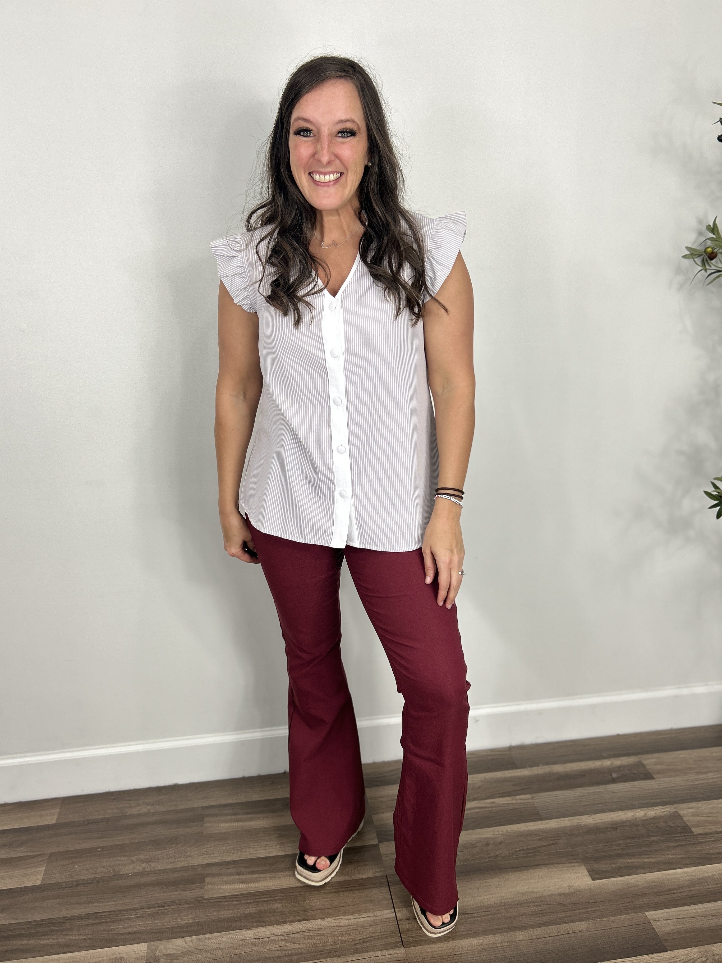 Women's grey and white pinstripe button up blouse with flutter sleeves paired with maroon flare pants and black wedge sandals.