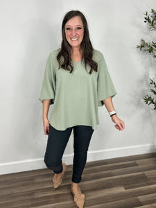 Women's v neck three quarter bubble sleeve top paired with charcoal skinny jeans and camel color flat shoes.