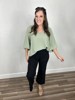 Load image into Gallery viewer, Women&#39;s v neck top in sage color side tucked into black denim wide leg pants styled with taupe wedges.
