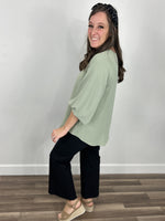 Load image into Gallery viewer, Side and back view of a woman&#39;s sage color 3/4 top paired with black denim pants and sandals.
