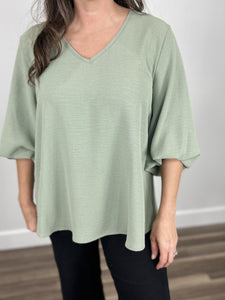 Upclose picture of women's sage green top with v neckline, wavy textured material, and 3/4 sleeves. 