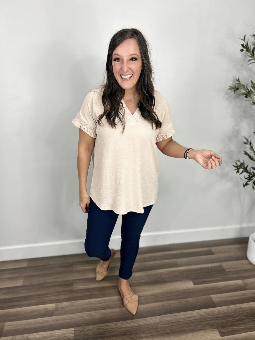 Women's cap sleeve v neck top in ivory paired with navy skinny jeans and camel color flat shoes.