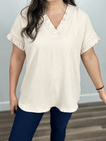 Load image into Gallery viewer, Upclose view of the Kara cap sleeve v neck top showing the slightly wavy texture as well as the ruching and ruffle on sleeve and neck.
