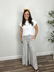 Multi color floral palazzo pants paired in a causal outfit with a white rolled cuff sleeves and black wedge sandals.