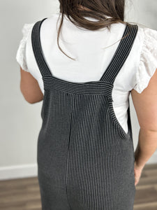 View of the shoulder straps on the Kobe Ribbed Comfort Jumpsuit in charcoal. Layered with a white flutter sleeve women's top.