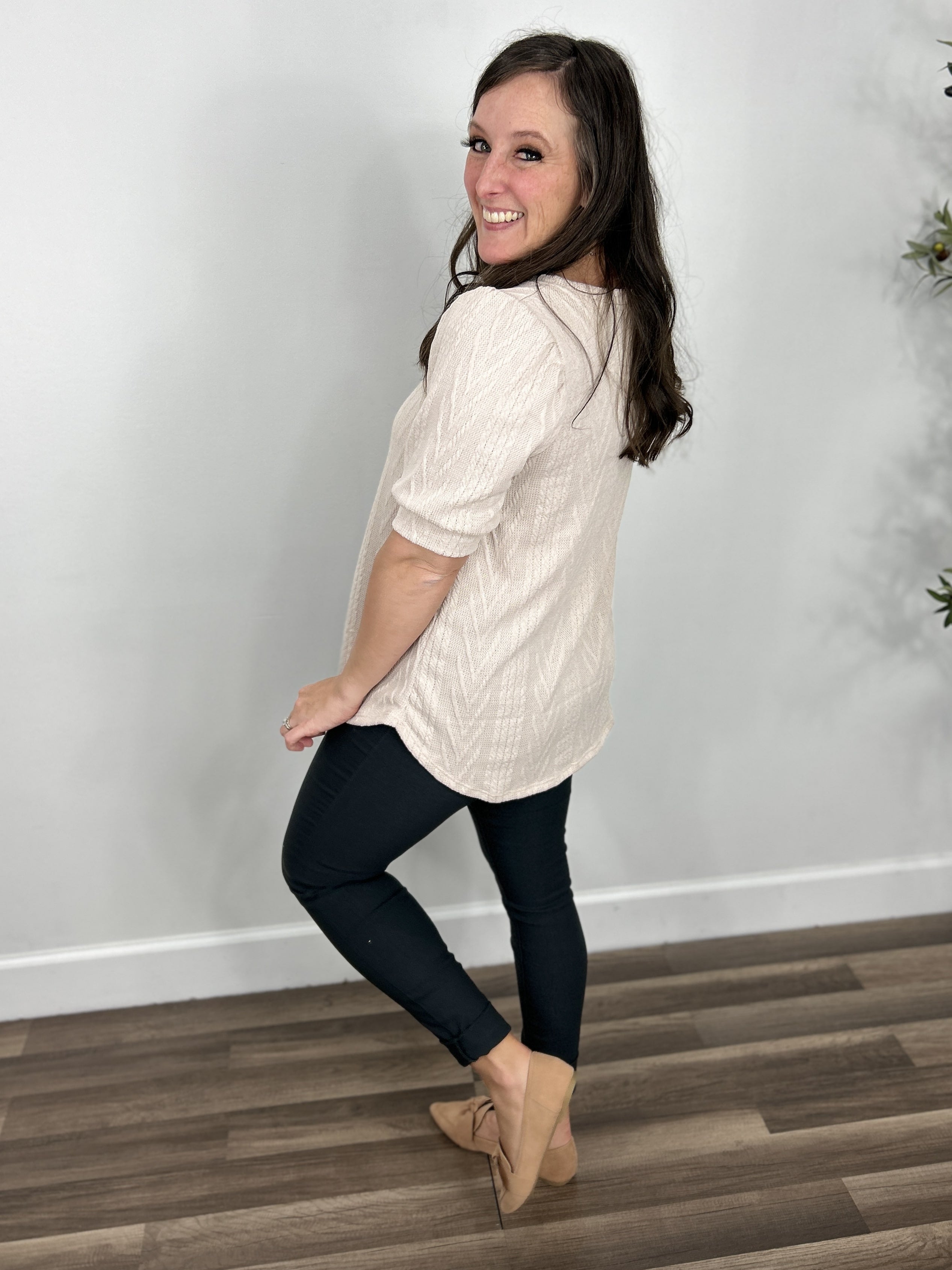 Side view of the women's lacy cable knit top in oatmeal paired with skinny pants and flat shoes.