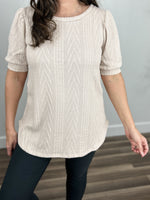 Load image into Gallery viewer, Detailed view of the cable knit fabric of the oatmeal color lacy top with a round neckline and curved hemline.
