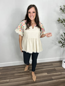 Outfit Styled- women's oatmeal color babydoll top with v neckline with embroidered flowers on short sleeves paired with charcoal skinny jeans and flat shoes.