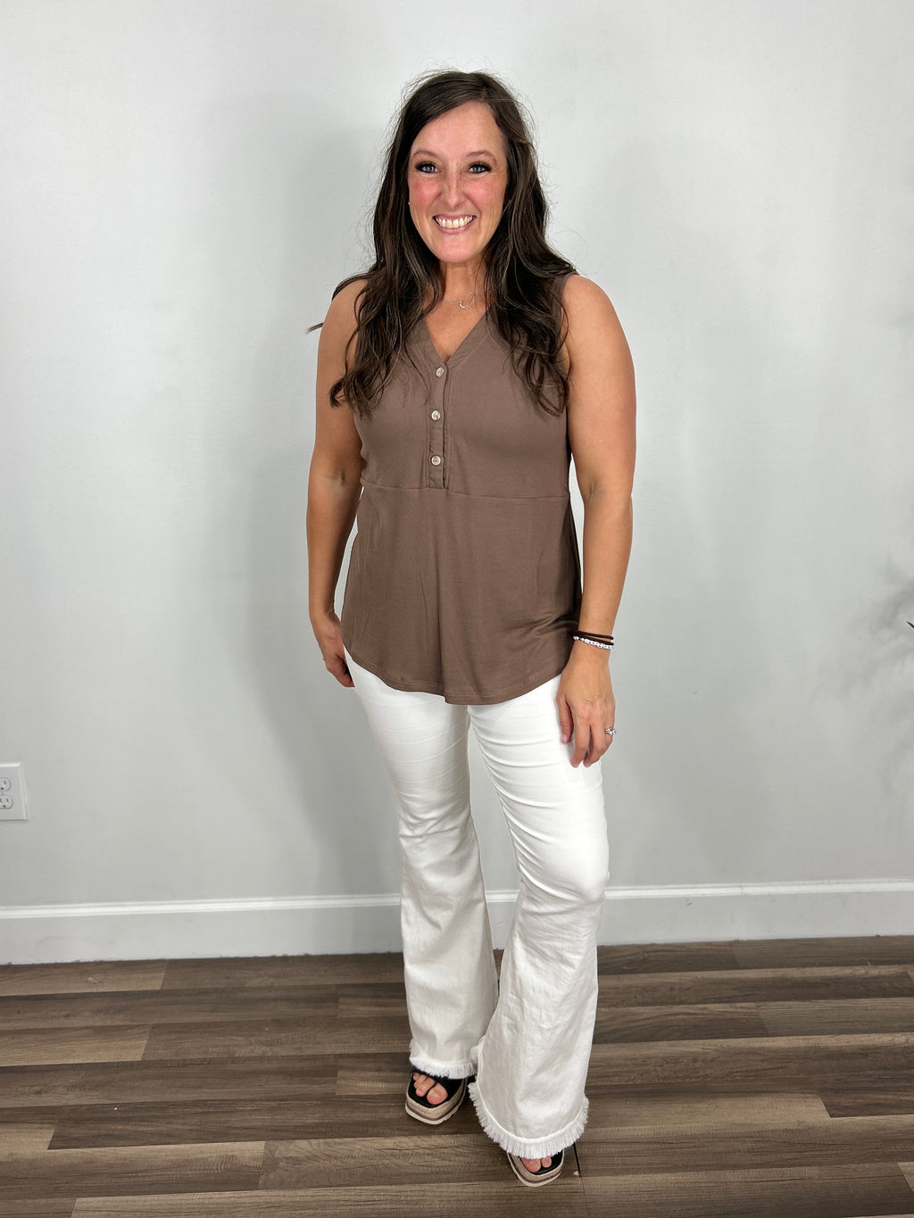 Women's brown sleeveless henley top paired with white flare pant and black wedge sandals.