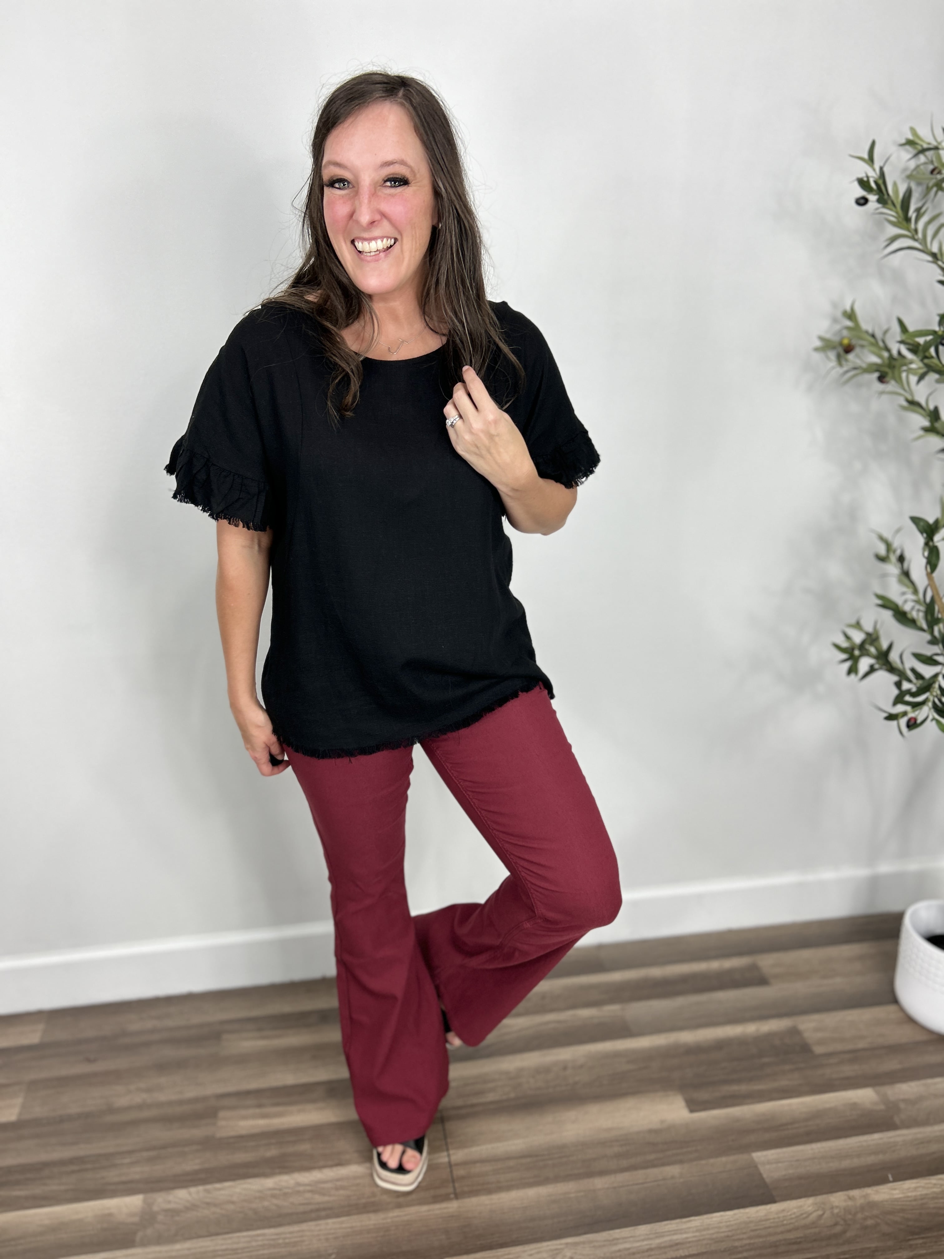 Women's black short sleeve top with back cutout paired with maroon flare pants and black wedge sandals.
