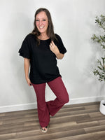 Load image into Gallery viewer, Women&#39;s black short sleeve top with back cutout paired with maroon flare pants and black wedge sandals.
