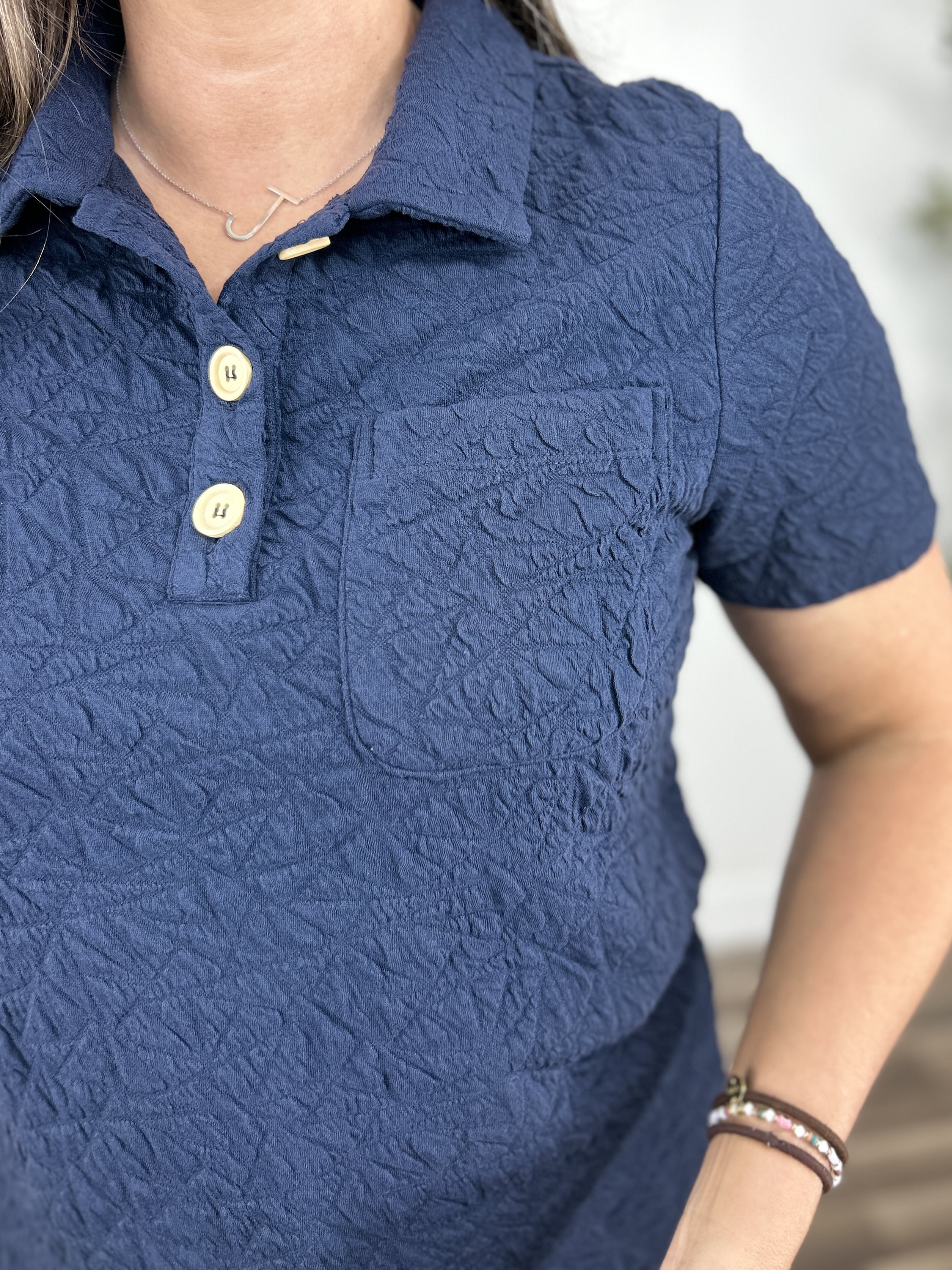 Upclose view of the women's navy blue textured henley top with 3 functional chest buttons and a singular chest pocket.