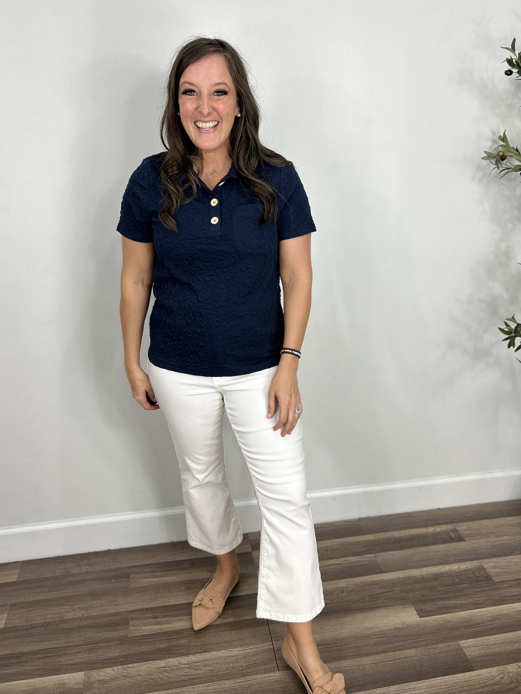 Women's navy blue textured short sleeve henley top paired with white crop flare pants and camel color shoes.