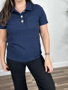 Close up view go the women's textured henley top in navy blue color with collared neckline dipping into a v neck with 3 functional buttons and a single left chest pocket.