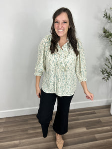 Lexie Flowery V Neck Ruffle Top front view sage and ivory flowers, neck ruffle and three quarter sleeves. Paired with black wide leg denim and flat taupe shoes.