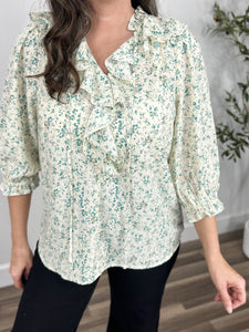 Upclose view of green and ivory flower shirt showing off the front ruffle that waterfalls from the shoulders down the front of the blouse.