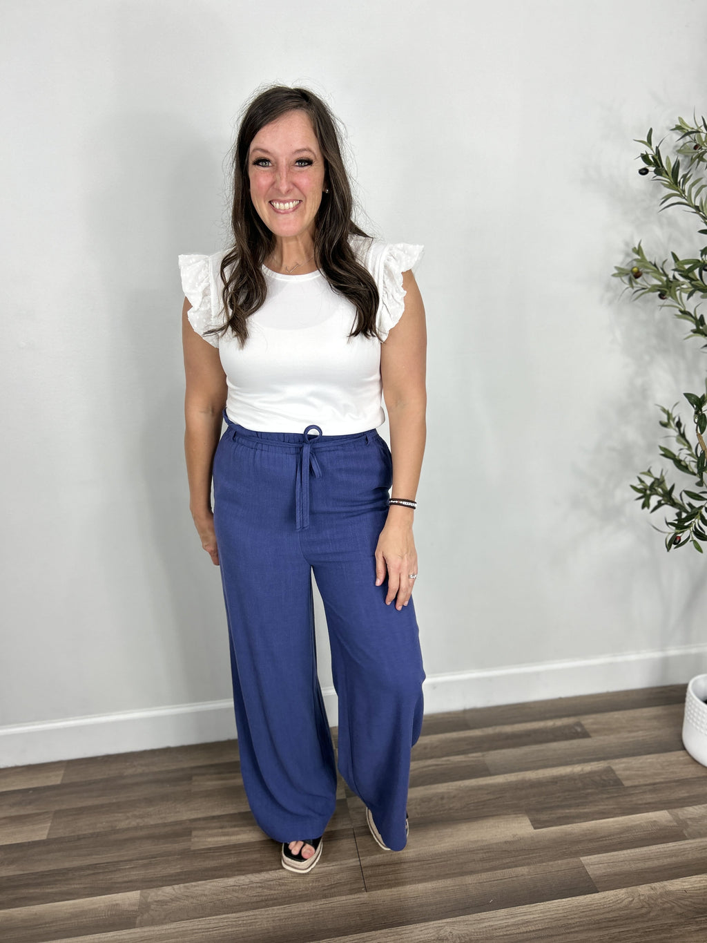 Women's ruffle sleeve white top paired with blue wide leg linen pants and Elvira black wedges.