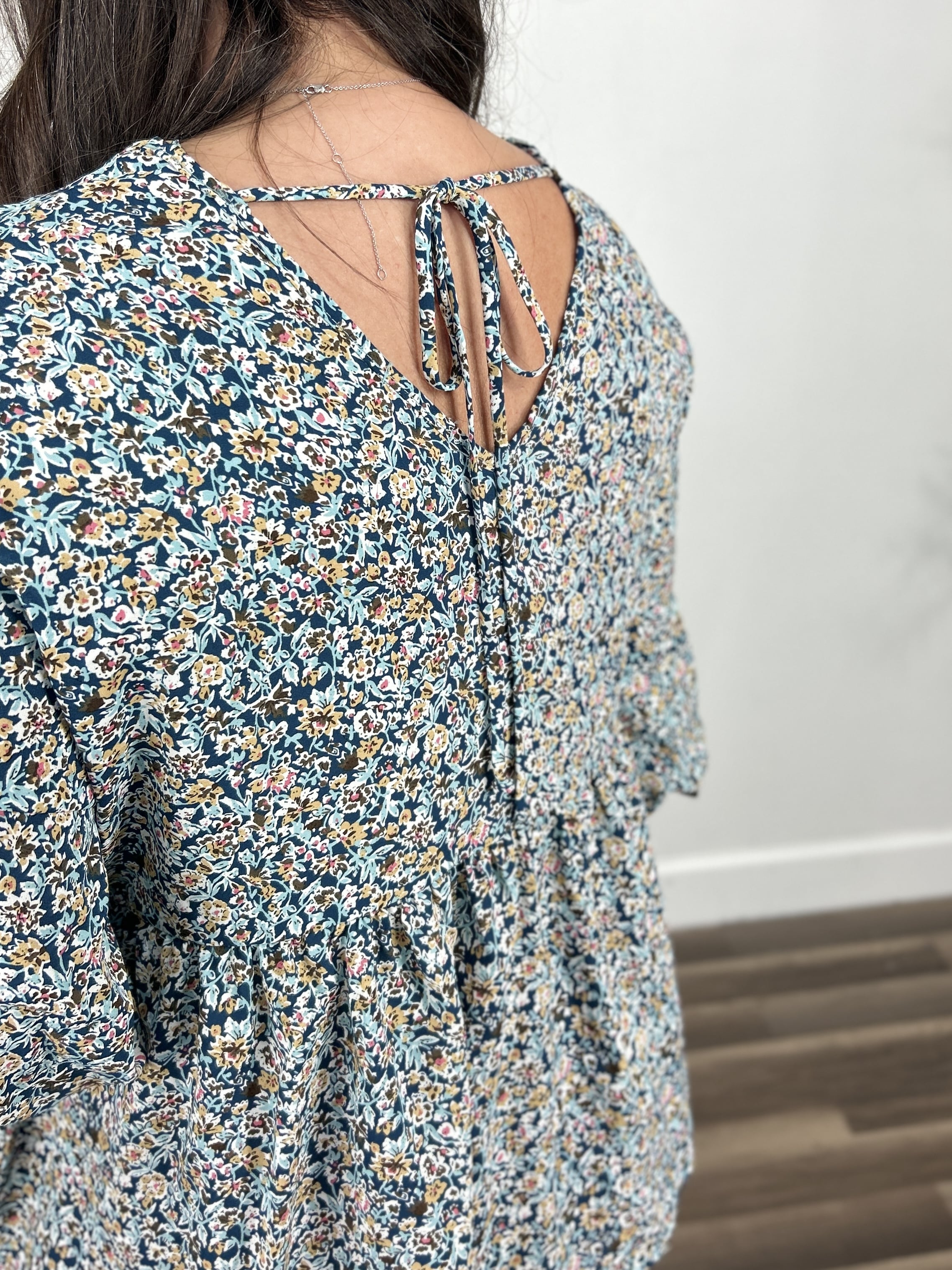 detailed view of the back of the women's floral top with a back v dip and a adjustable tie.