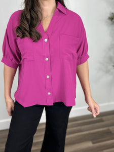 Upclose view of the women's magenta color puff short sleeve top with collared neckline that dips into a v then buttons down he center.