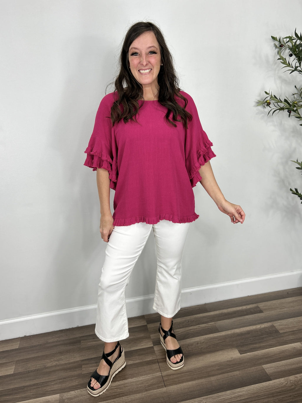 Women's fuchsia Meredith linen ruffle sleeve top paired with white crop pants and black sandals.