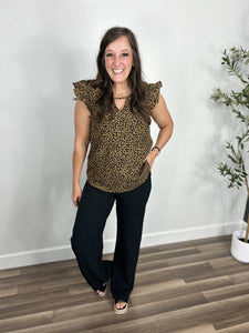 Women's leopard print ruffle sleeve top paired with black dress pants and black wedge sandals.