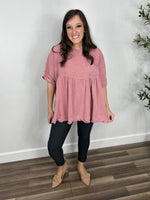 Load image into Gallery viewer, Women&#39;s mineral wash pink short sleeve oversized babydoll top paired with charcoal skinny jeans and paired with camel color flat shoes.
