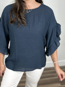 Upclose view of the crinkle material on the Rigsby three quarter ruffle sleeve top in navy with a round neckline and straight hemline.