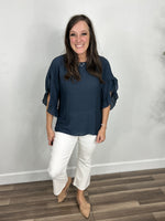 Load image into Gallery viewer, Women&#39;s navy three quarter ruffle sleeve top paired with white crop pants and camel flat shoes.
