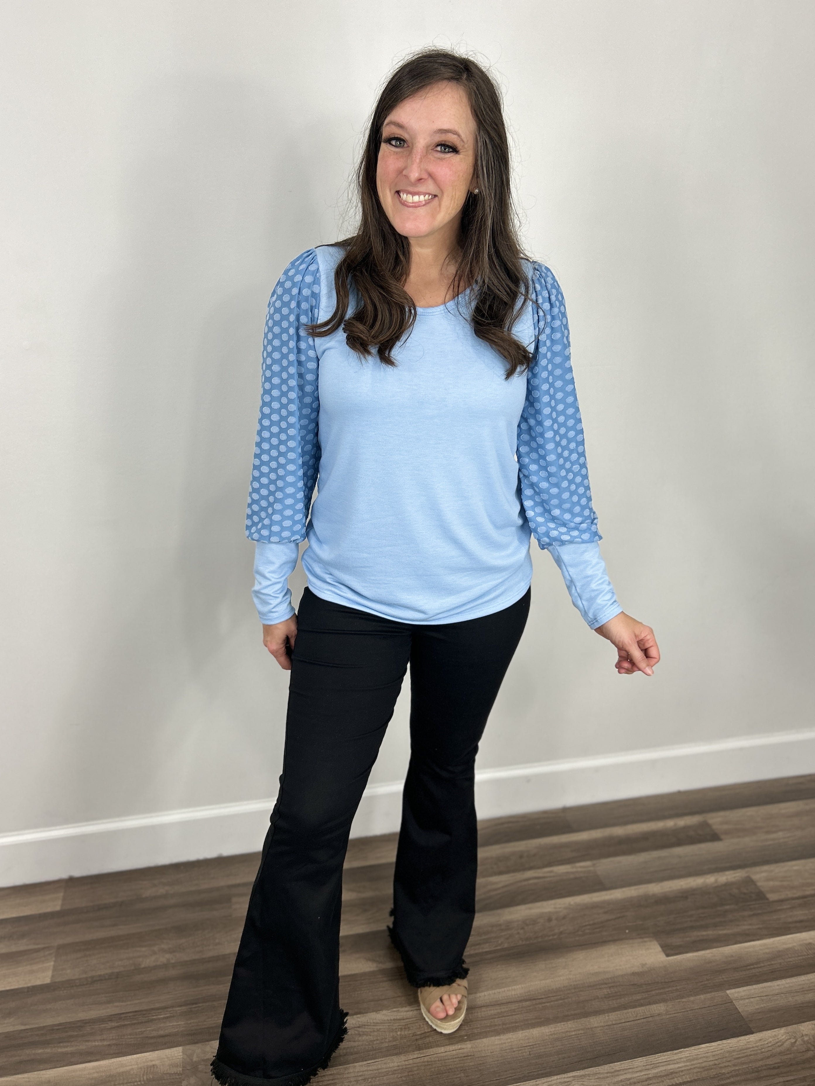 Women's blue top with dotted long sleeves paired with black flare pants and taupe sandals.