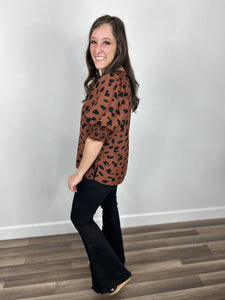 Women's black and brown large leopard print pattern top side view of side slits and puff short sleeves paired with black flare leg pants.